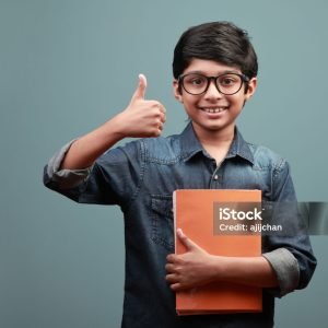 Smiling boy holding note books in hands shows a thumbs up gesture